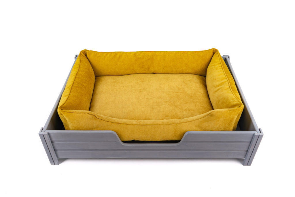 panier pour chien en velours jaune sur un support en bois gris avec pattes sur fond blanc.