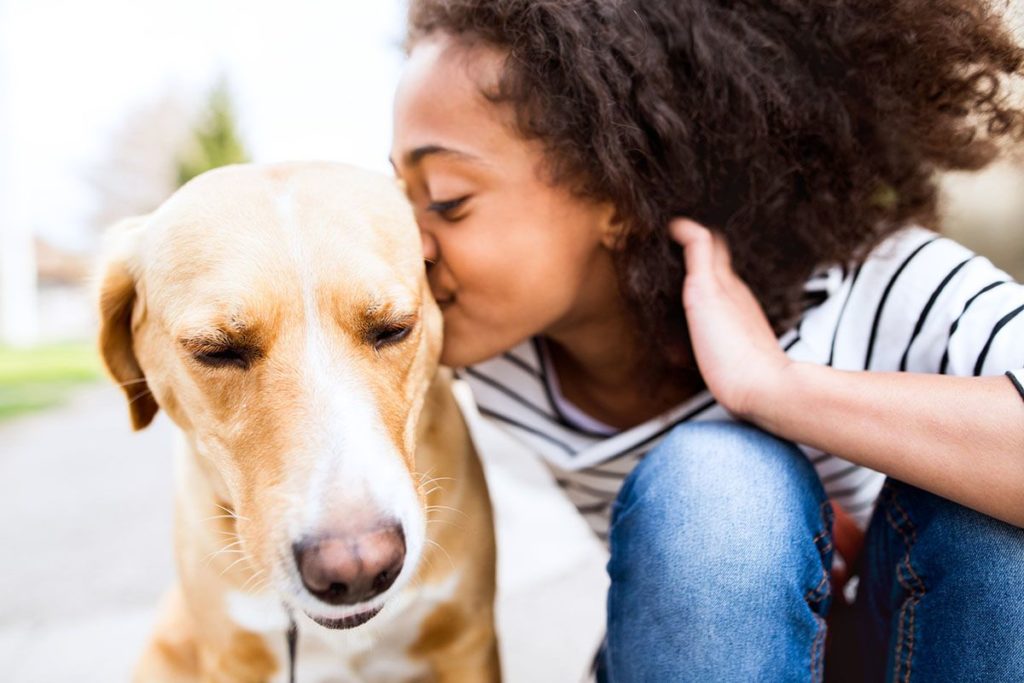 Une fille métisse qui embrasse son chien beige. Le chien pleure de joie.