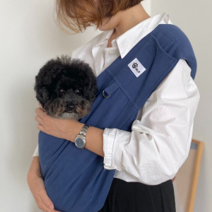 chien installé dans un sac de transport pour chien bleu en écharpe , dans les bras de maitresse