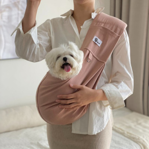 chien blanc installé dans un sac de transport pour chien rose en écharpe, dans les bras de sa maitresse